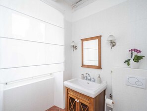A bathroom with a window, a sink, a mirror, and a wall-mounted light fixture. - Secret Apartments - Two Bedroom Apartment With City View (Dubrovnik)