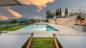 A modern outdoor pool area with a clear view of the surrounding landscape, including distant mountains and a stone wall with steps leading up to a balcony.