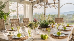 A dining table set for six with wicker chairs, green apples, and glassware.