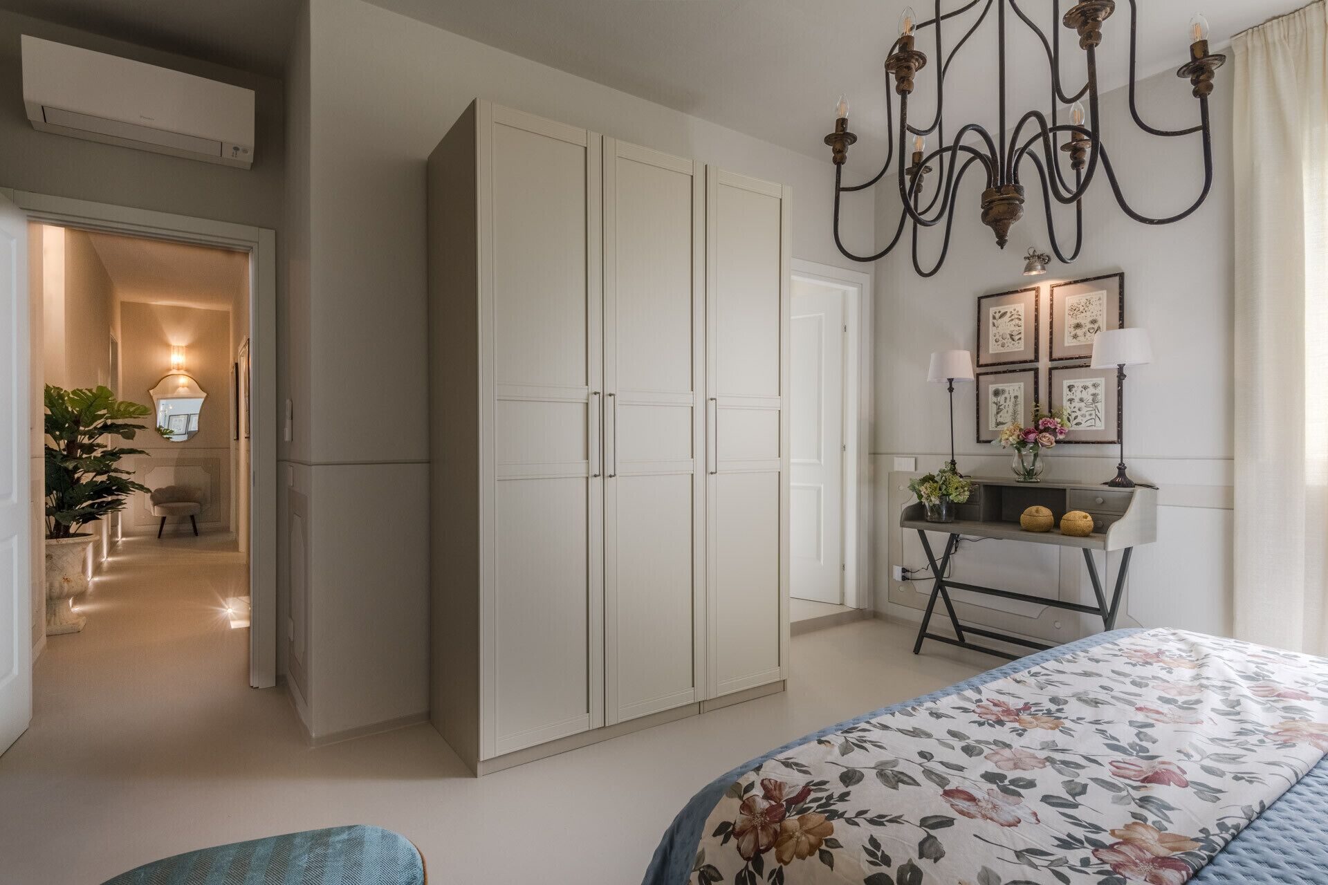 A bedroom with a large wardrobe, a bedside table with lamps, and a floral bedspread.