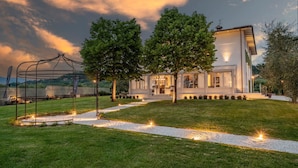 A modern house with a spacious front yard, a pergola, and a well-maintained lawn.