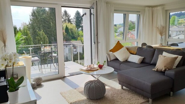 En moderne stue med en grå sofa, et sofabord og en balkon med bord og stole.