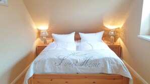 Una cama bien hecha con una colcha blanca y almohadas, dos lámparas de noche y un cabecero de madera.