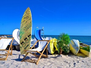 Una playa con sillas de descanso, una tabla de surf y una pequeña palmera.