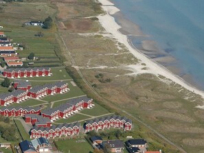 A coastal residential area with red houses arranged in rows, a sandy beach, and a clear view of the sea. - 6 Person Holiday Home in Hadsund (Hadsund)