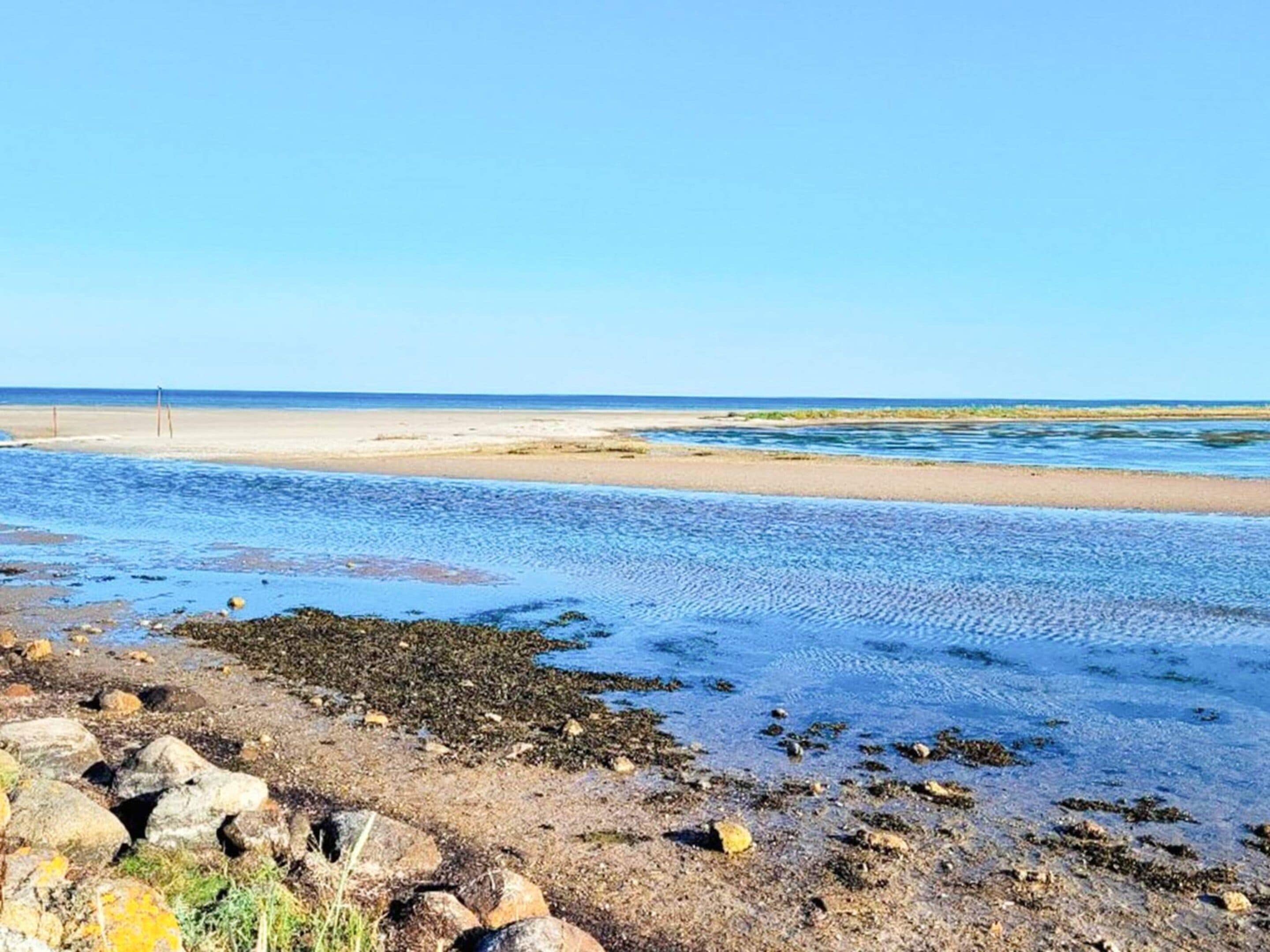 Una playa con agua cristalina, rocas y una costa lejana.