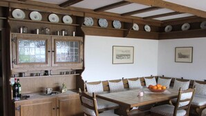 A dining area with a wooden table and chairs, a cabinet with dishes, and a window. - With Lake and Alpine View (Immenstaad am Bodensee)