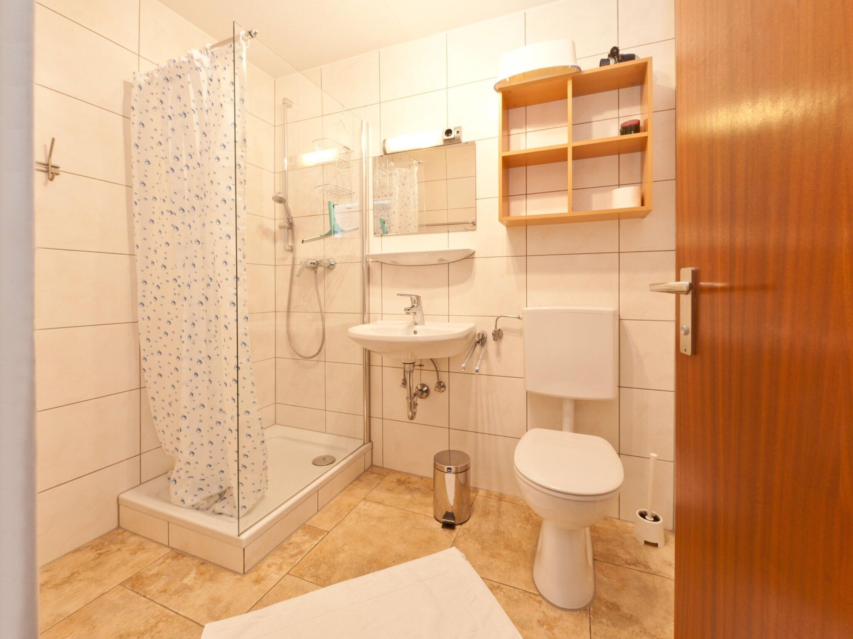 Un bagno con doccia, lavandino, WC e uno scaffale in legno sopra il water.
