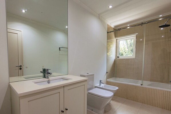 Ein modernes Badezimmer mit einem großen Spiegel, einem Waschbecken, einer Toilette, einem Bidet und einer Badewanne.
