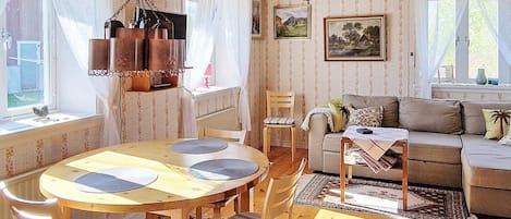 Ett mysigt vardagsrum med ett träpanelat tak, ett matbord med stolar, en soffa och en kristallkrona.