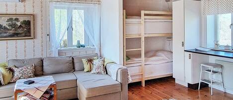 A cozy room with a sofa, a bunk bed, a desk, and a window.