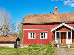 A red wooden house with a tiled roof, a small porch, and a visible chimney.