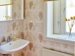A bathroom with a white sink, a mirror above it, and a window with a view of trees.