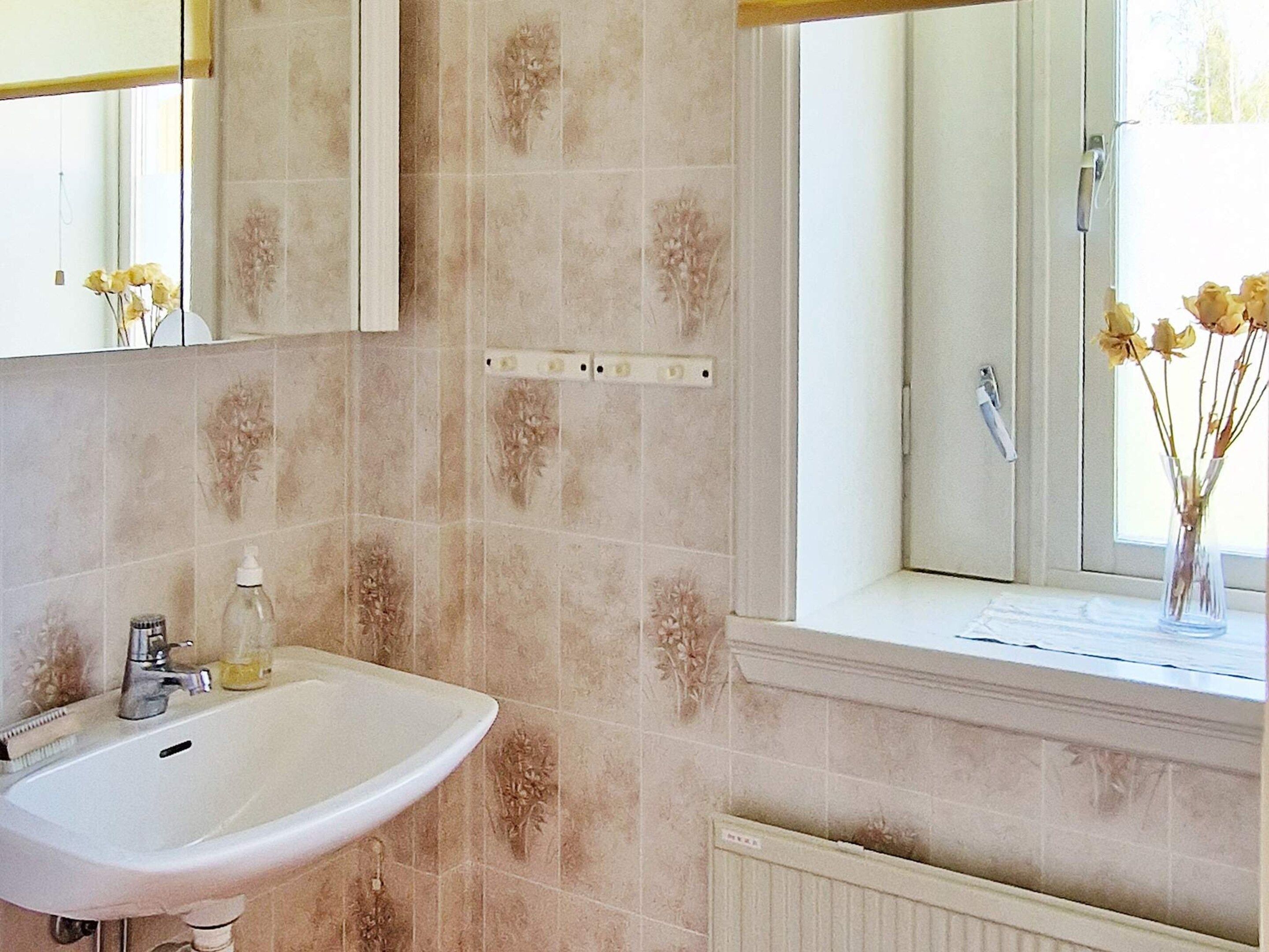 A bathroom with a white sink, a mirror above it, and a window with a view of the outside.