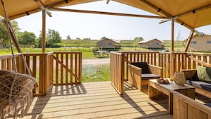 A wooden deck with a swing chair and a table with a basket and glass of orange juice. - Safari Lodge Near Ijsselmeer Glamping (Andijk)