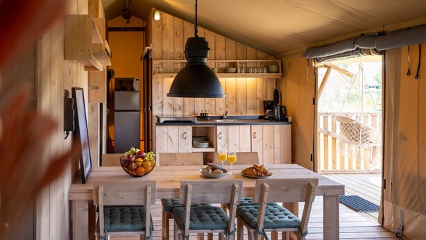A wooden interior with a dining table, chairs, and a hanging light fixture. - Safari Lodge Near Ijsselmeer Glamping (Andijk)