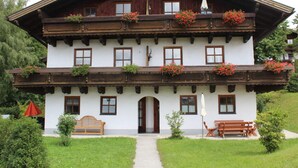 Una cabaña tradicional con fachada de madera, varios balcones con jardineras y una entrada principal con banco y mobiliario de exterior.
