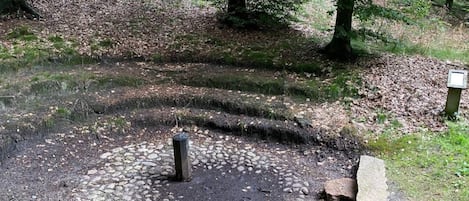 Ein bewaldetes Gebiet mit einem kreisförmigen Muster aus Steinen, einer Steinsitzbank und einem Wegweiser.