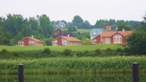 Reihle an roten Häusern mit großen Fenstern vor einer Kulisse aus üppiger Vegetation und ruhigem Gewässer.