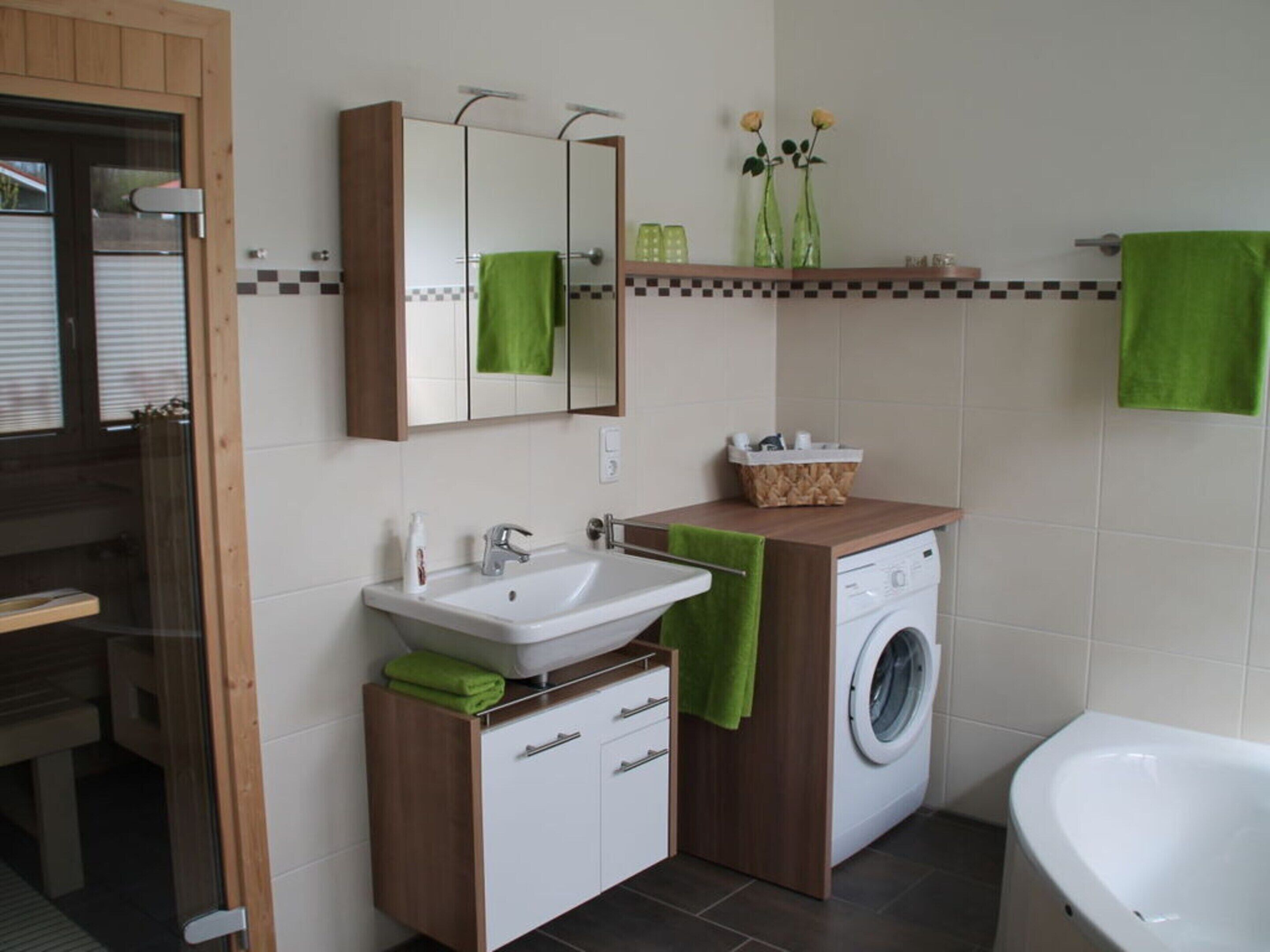Une salle de bain moderne avec un lavabo, un miroir, des serviettes vertes, un lave-linge et une baignoire.