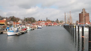 Ein Hafen mit vertäuten Booten, ein markantes rotes Gebäude und eine hohe Struktur auf der rechten Seite.