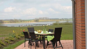 Eine Terrasse mit Tisch für Zwei, mit Blick auf einen See und Wiesen.