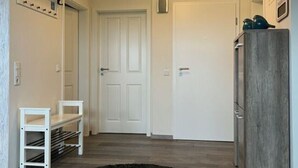 A hallway with a white door, a coat rack, a small table, and a dark rug. - Holiday Apartment Ponywiese (Ihlow)