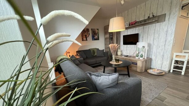 A modern living room with a sofa, coffee table, and a TV mounted on the wall. - Holiday Apartment Ponywiese (Ihlow)