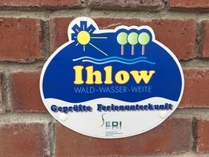 A sign with the text "Ihlow Wald-Wasser-Weite" and "Geprüfte Ferienunterkunft" on a brick wall. - Holiday Apartment Ponywiese (Ihlow)