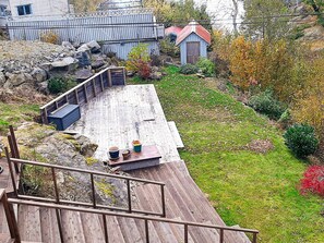 Eine Holzterrasse mit Geländer, einem kleinen Tisch mit Gegenständen sowie ein Garten mit Steinen und Pflanzen.