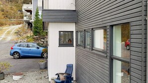 Un edificio moderno con fachada gris y sección blanca. Un coche azul está estacionado adelante, y una silla colocada afuera.