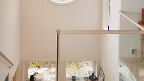 Una habitación con techos altos, piso de madera, ventana con vista a un jardín y una pequeña mesa con velas y un farol.