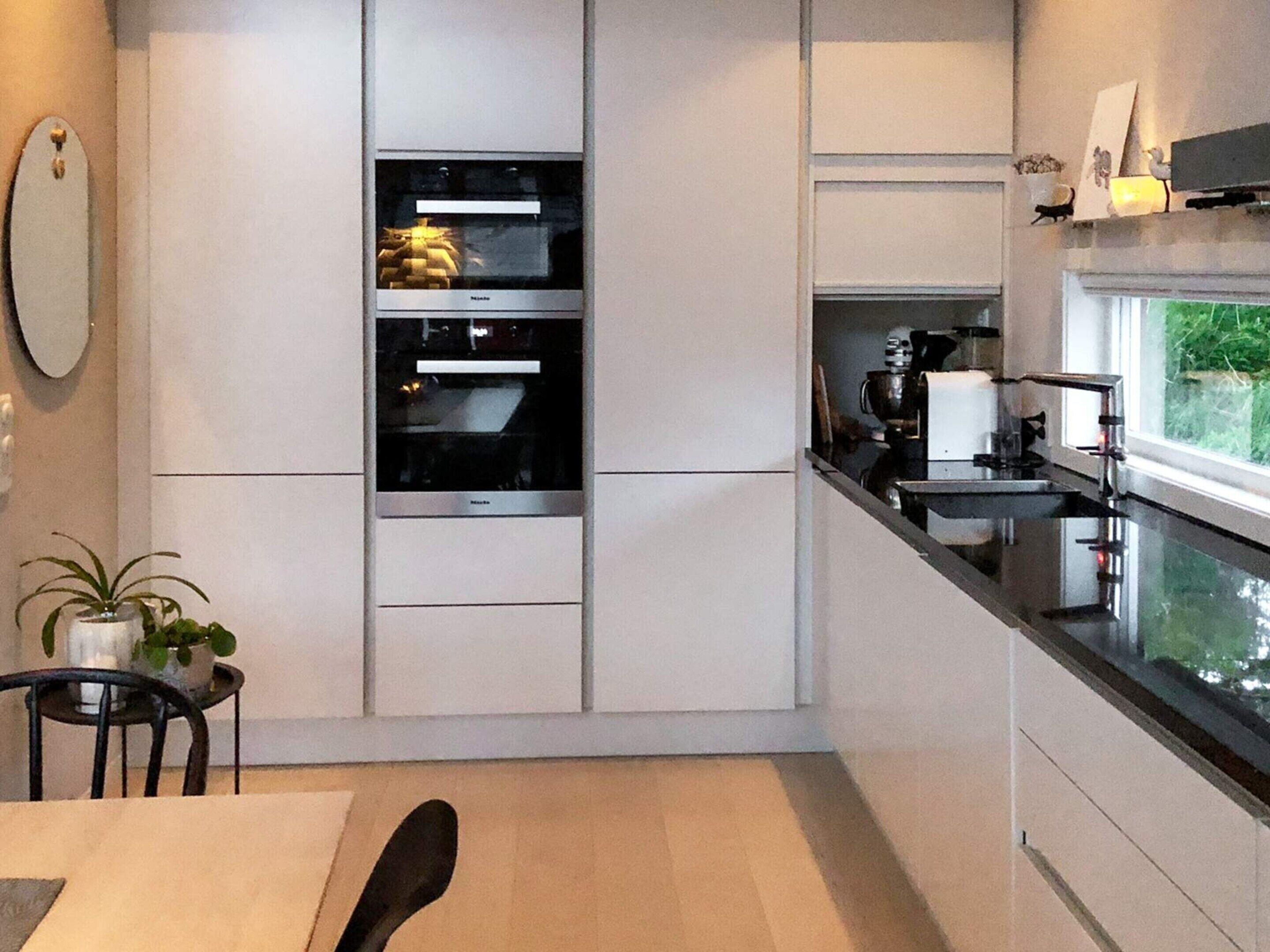 A modern kitchen with built-in appliances, a dining area with a table and chairs, and a view of greenery outside.