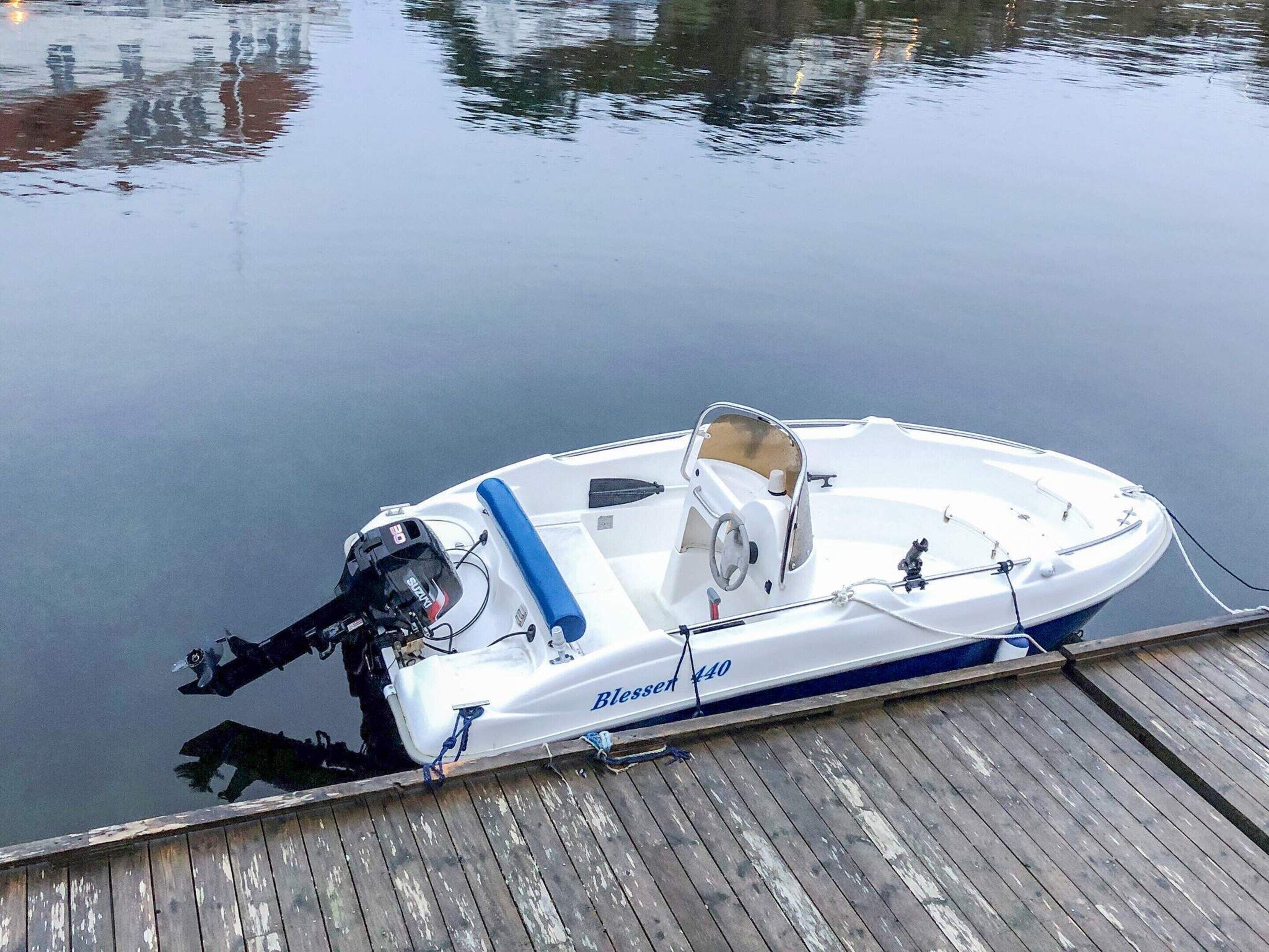 A small white boat named 'Blesset 440' docked at a wooden pier.