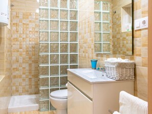 Un bany amb un envà de dutxa de vidre, un vàter blanc i un lavabo amb una pila de tovalloles.