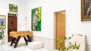 Una habitación con mesa de fútbol, una mesa de vidrio con planta, un sofá y obras de arte en las paredes.