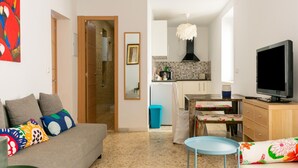 Una sala de estar con un sofá, una televisión y una zona de cocina con salpicadero de azulejos.