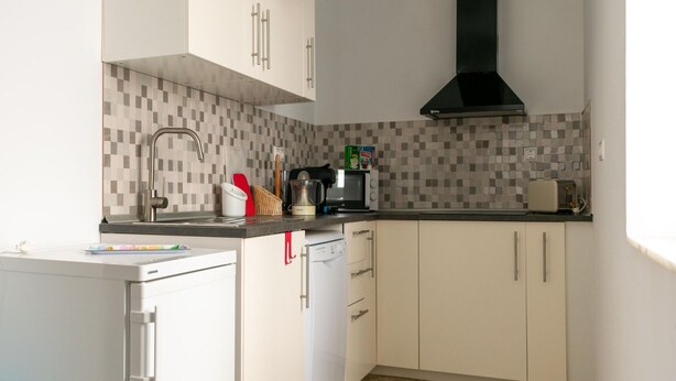 Cocina moderna con armarios blancos, salpicadero de azulejos, lavavajillas, fregadero y campana extractora negra.