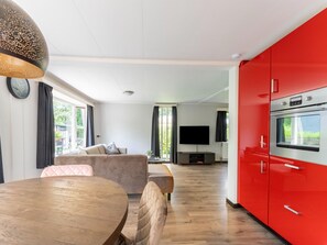 Una sala moderna con sofá, una mesa de comedor y una zona de cocina con armarios rojos y horno empotrado.