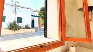 A bathroom with a window view of a building with a white facade and green shutters. - Belvilla by OYO Villa Cepillo I (Nijar)