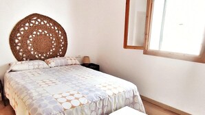 A bedroom with a bed, a nightstand, a lamp, a wooden headboard, a window, and a white bench. - Belvilla by OYO Villa Cepillo I (Nijar)