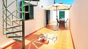 A narrow outdoor corridor with a spiral staircase, a table with chairs, and a large umbrella. - Belvilla by OYO Villa Cepillo I (Nijar)
