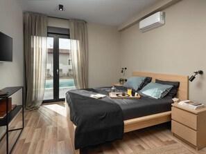 A modern hotel room with a bed, bedside tables, a TV, and a view of a swimming pool. - Cosy Apartment in Istria (Vodnjan)