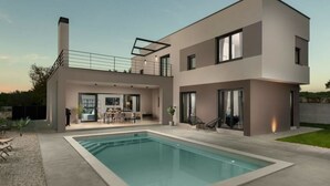 Una casa moderna de dos pisos con piscina, mobiliario exterior y un amplio acceso por puerta de vidrio.