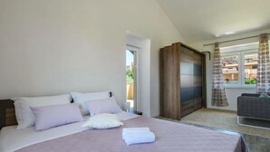 A neatly arranged bedroom with a large bed, a wooden wardrobe, and a view of the outside through a window with curtains. - Boky Comfortable Holiday Residence (Vodnjan)