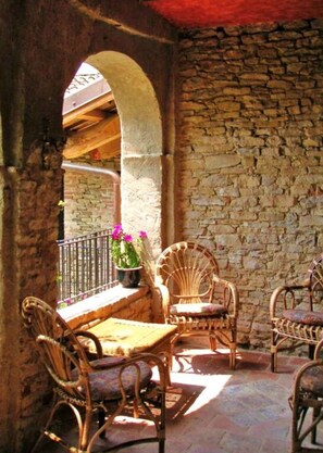 An outdoor patio with wicker furniture, a stone wall, and a view of a building in the background. - Nice Apartment in Trassenheide (Bonvicino)