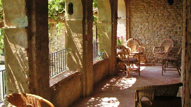 A covered outdoor seating area with stone walls and arches, wicker furniture, and hanging lanterns. - Nice Apartment in Trassenheide (Bonvicino)