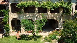 A stone building with a tiled roof, arched windows, and a courtyard with potted plants and a bench. - Nice Apartment in Trassenheide (Bonvicino)