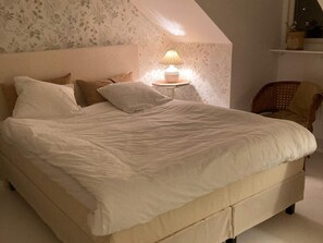 Une chambre avec un grand lit, une table de chevet avec une lampe et une chaise.