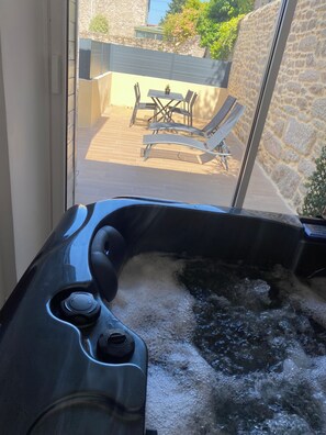 A hot tub with a control panel, a stone wall, and a patio area with a table and chairs. - Maison Rénovée Avec un Jacuzzi Privatif. A 7 Minutes à Pieds du Centre-ville (Dinan)